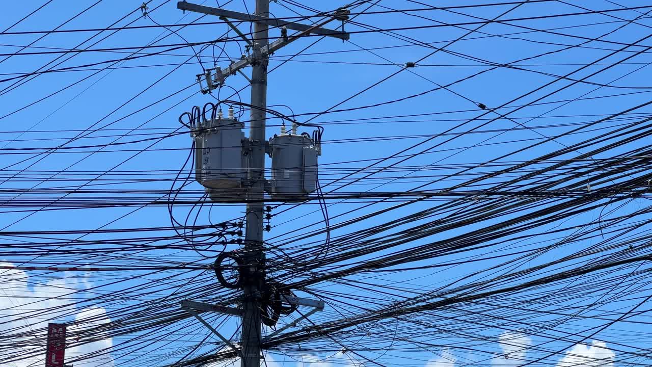 Close-up of tangled electrical lines and transformers on a city pole under a clear sky—perfect for infrastructure, energy, or technology themes