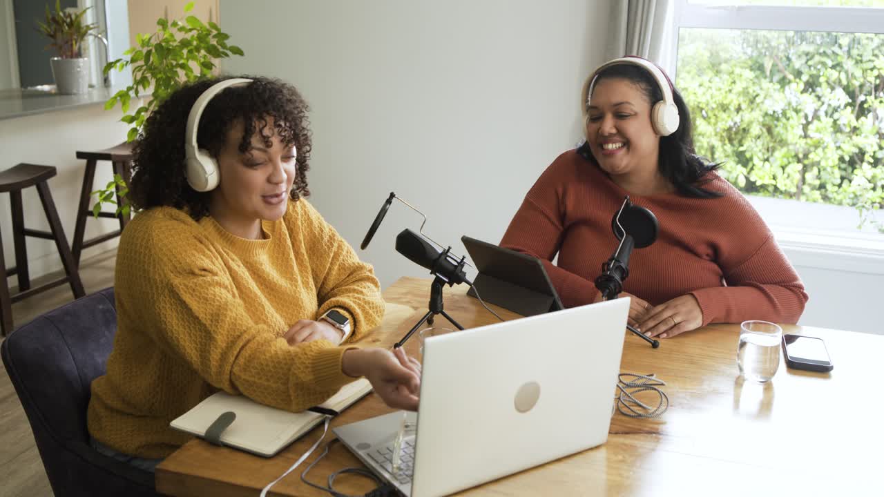 Female co-hosts starting podcast recording, adjusting mics, typing notes at home office