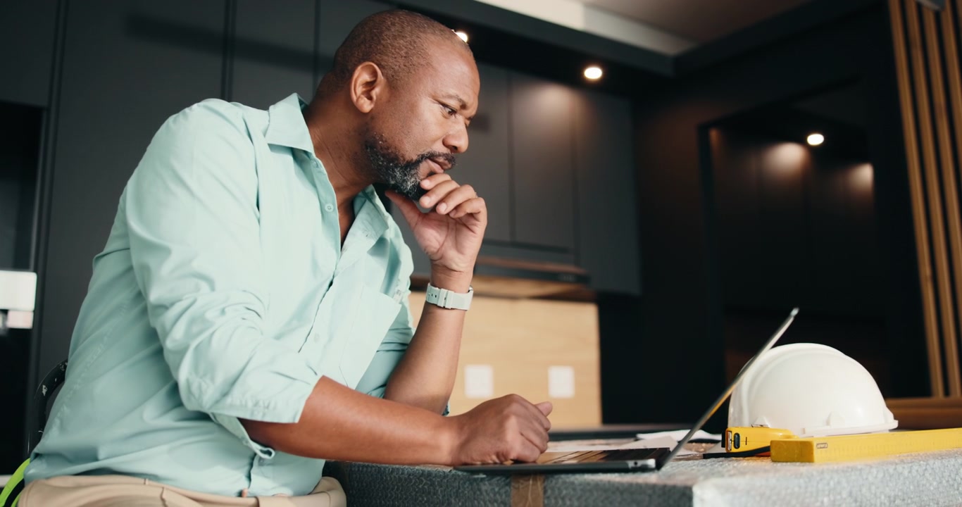 Architect Reviewing Blueprints on Laptop in Modern Kitchen