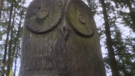 escultura de búho en primer plano en el bosque inglés con la luz del sol cayendo sobre la escultura y una panorámica muy lenta