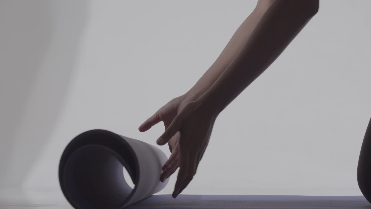 manos de mujer vistas desplegando una alfombra de yoga para hacer ejercicio - silueta aislada con fondo brillante