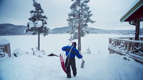 man at work carrying traditional and modern snow sled shovel