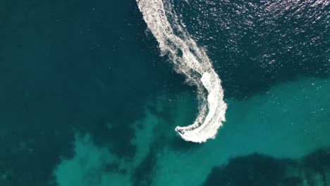 Aerial-Shot-above-fast-several-jet-skis,-going-around-in-circles-beaking-white-foam-in-the-vast-blue-sea-near-Ibiza,-Spain