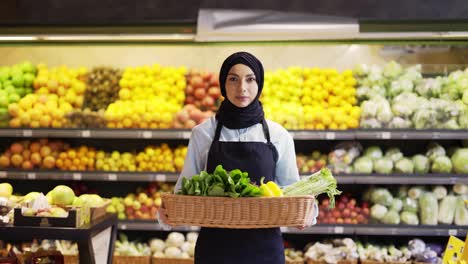 portrait of a woman in hijab standing with basket of fresh vegetables and greens in the supermarket