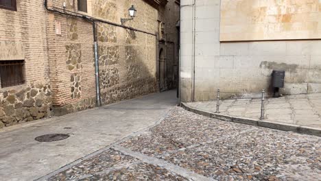 filming on a street in toledo where we see a cobbled floor and raising the camera we see the magdalena church from the 12th century in mudejar style, we see its entrance porch and its bell tower