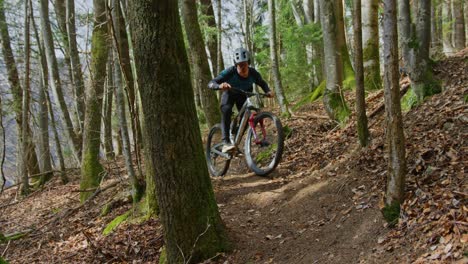 Ein-Mountainbiker-Fährt-Eine-Enge-Kurve-Durch-Schmale-Bäume-In-Einem-Laubwald