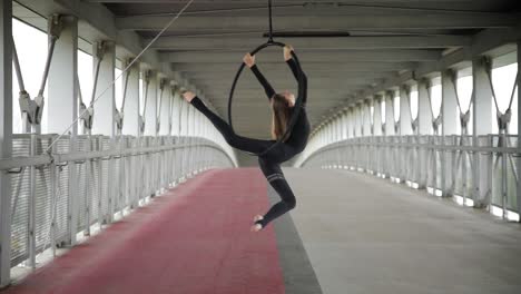 Flexible acrobat balancing on a hoop hanging on a street bridge
