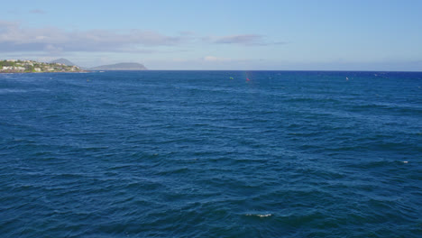 drone footage of the royal blue pacific ocean water dotted with kite boarders and surfers enjoying the beautiful weather in hawaii