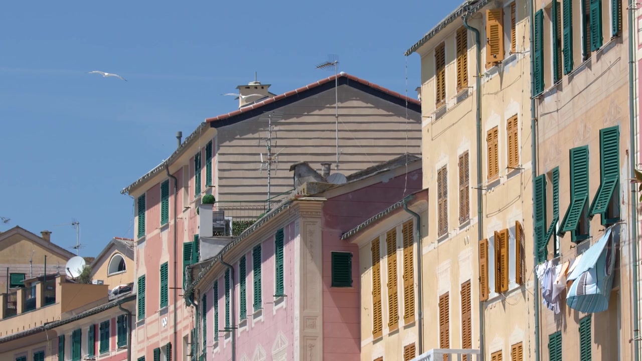 Una lenta panoramica della telecamera attraverso vivaci facciate mediterranee con persiane verdi sotto la luce del sole splendente.