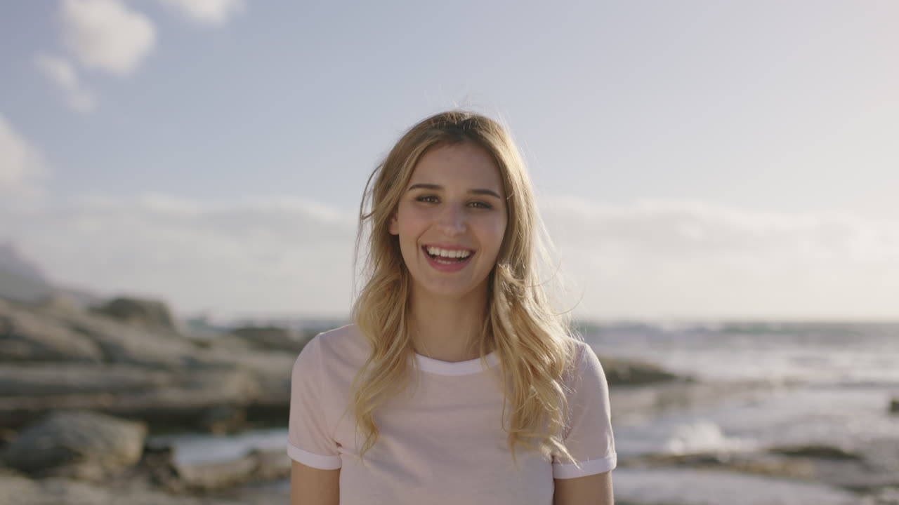 Portræt af smuk blond kvinde, der griner muntert på stranden på en solrig dag.