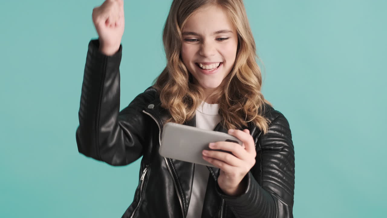 Teenage Caucasian girl in leather jacket playing online games on her smartphone and winning.