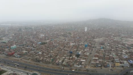 Drohnenaufnahme-Einer-Massiven-Und-überfüllten-Nachbarschaft-Neben-Einer-Autobahn-In-Ventanilla-Im-Bezirk-San-Juan-De-Miraflores