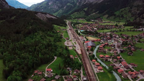 Vuelo-Sobre-Un-Valle-De-Montaña-Suizo-Alrededor-De-Las-Vías-Del-Tren-Con-Un-Tren-De-Coches-Para-Hacer-Cola-Para-El-Túnel-De-Lötschberg