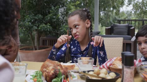 happy biracial parents, son and daughter eating meal at dinner table in garden, slow motion