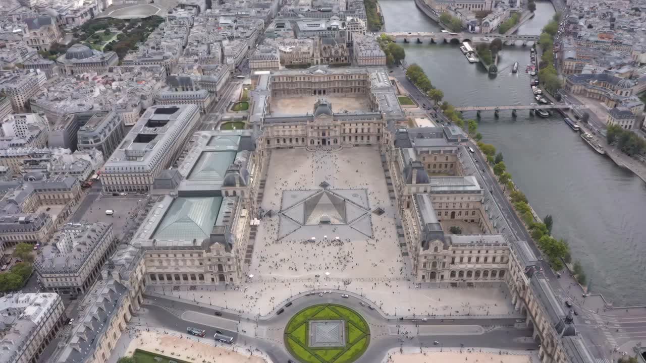 Aerial drone view descending over the Louvre with Pyramid, Tuileries Garden, Seine River and Place du Carrousel surrounded by the historic Parisian skyline