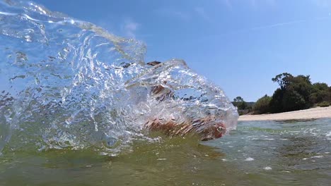 niño caucásico jugando en el mar moviendo las manos para crear salpicaduras, cámara lenta
