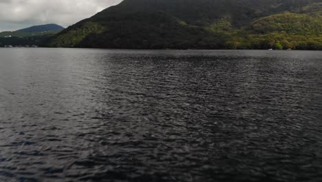 slow moving cinematic tilt up aerial drone close to water level towards hills with green forest and sky