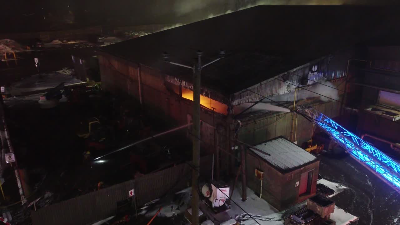 Firefighters working to put out a fire in an industrial building in the middle of winter with ladder trucks at night, aerial