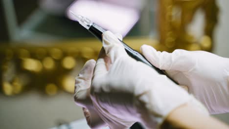 a beautician in white gloves holds pen in her one hand, and other adjusts the device for permanent makeup in a beauty salon before the arrival of the client.