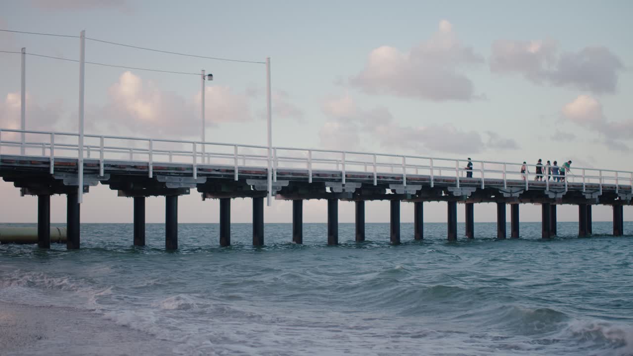 튼튼하게 지어진 부두는 석양에서 쏟아지는 빛의 파란색과 분홍색 파스텔 색상을 반사하기 때문에 쌀쌀한 해변 물을 가로질러 뻗어 있습니다.