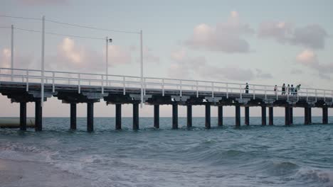 un muelle de construcción robusta se extiende a lo largo del agua fría de la playa, ya que refleja los colores pastel azul y rosa de la luz que se derrama desde el sol poniente