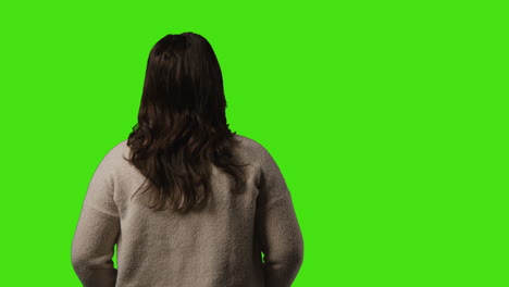 rear view of bored or fed up young woman standing and waiting against green screen background 1