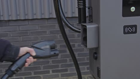 hand grabbing the plug of an electric vehicle charging station and placing it back