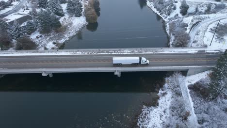 semi truck driving across a bridge with snow covering the ground