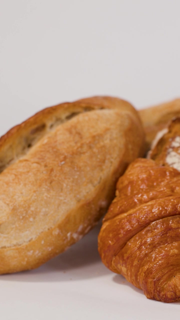 Close-up shot of hand arranging artisanal bread and croissant on white background with bright lighting.