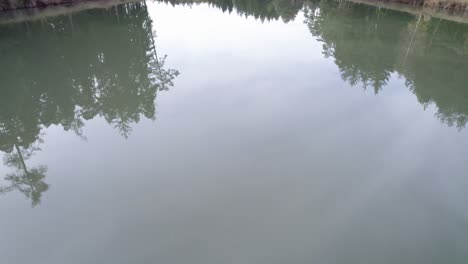 Aerial-footage-flying-over-a-lake-and-gradually-revealing-a-wooden-shed-used-for-boat-storage