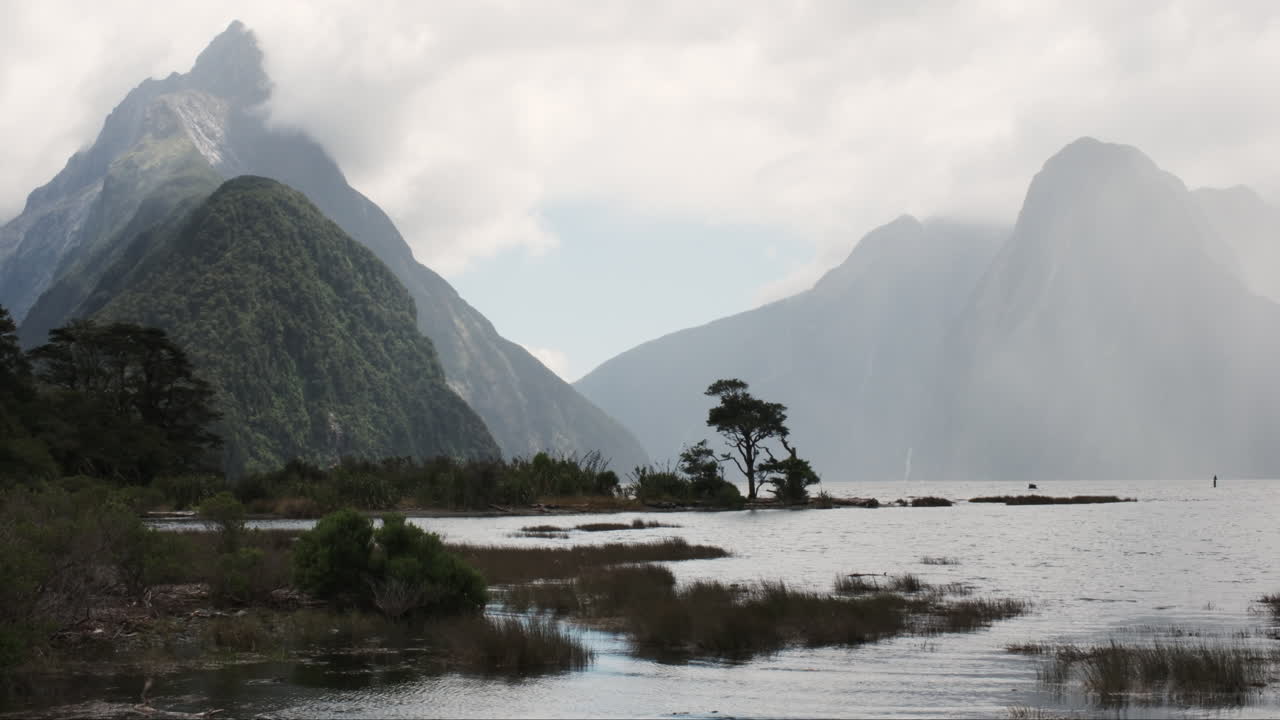 Panorama of Milford Sound, majestic cloud-shrouded peaks rise from the depths of a mirror-like fiord