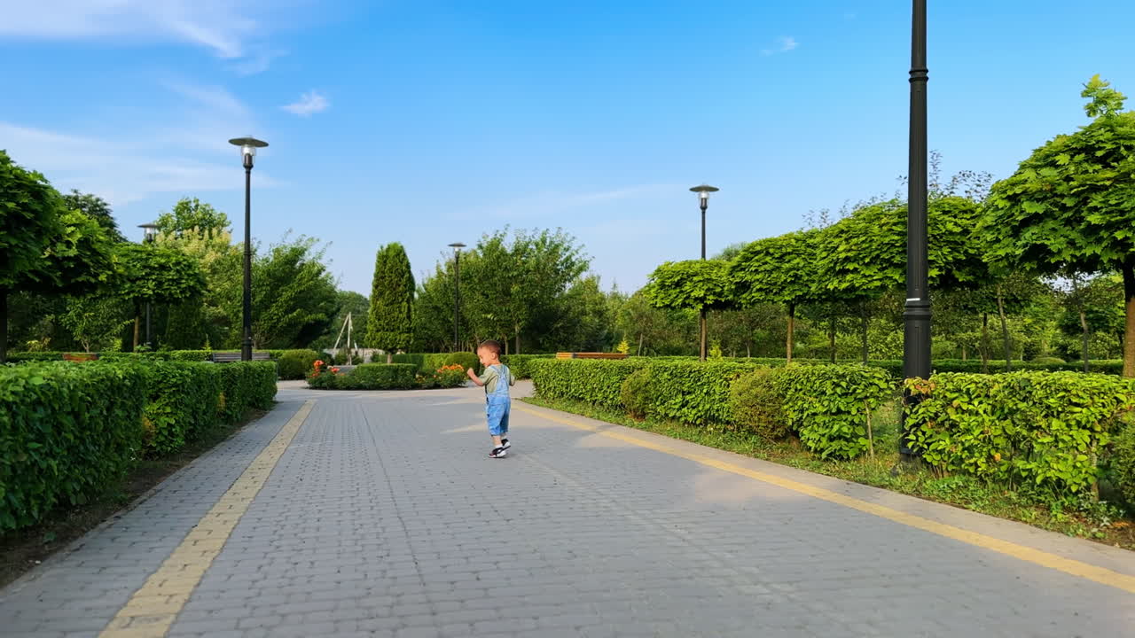 Happy smiling cute kid running cheerfully outdoors. Adorable Caucasian kid runs by the park in summer.