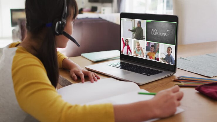 Scolara che usa il laptop per una lezione online a casa, con un'insegnante di diverse origini e la classe sullo schermo