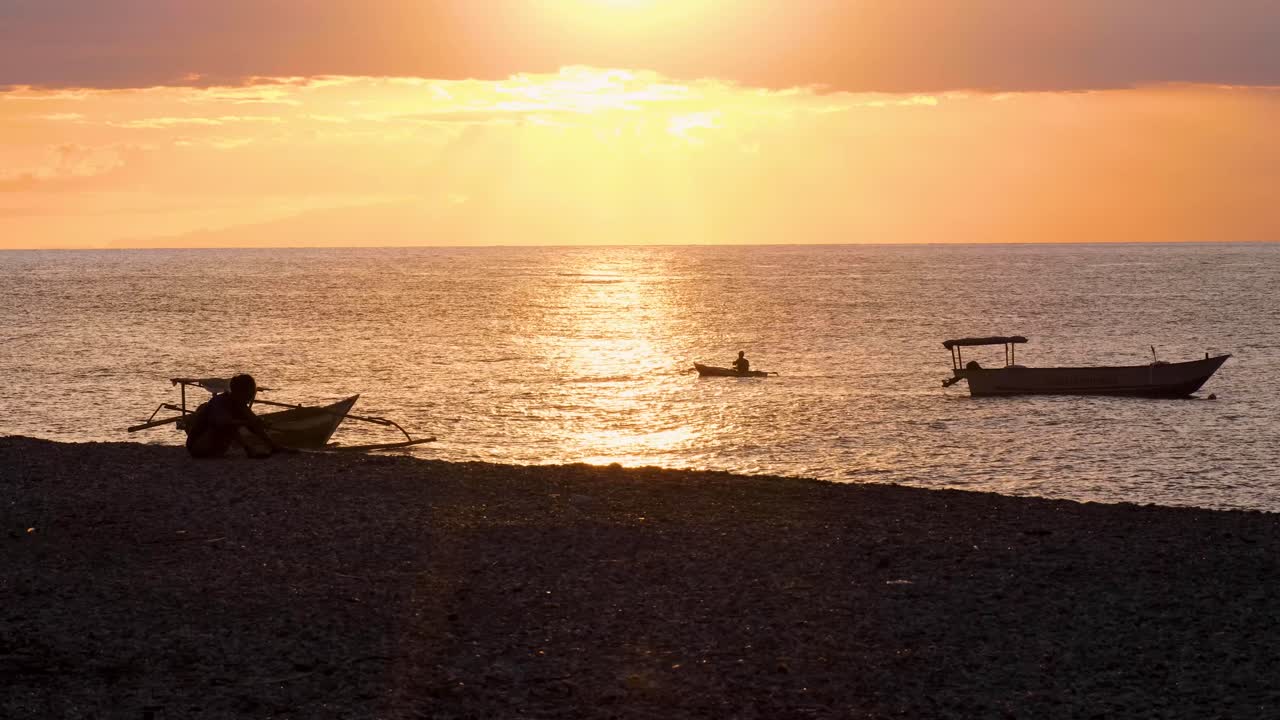 Local fisherman in a traditional fishing canoe paddling in ocean during beautiful golden sky sunset on tropical island of Timor-Leste