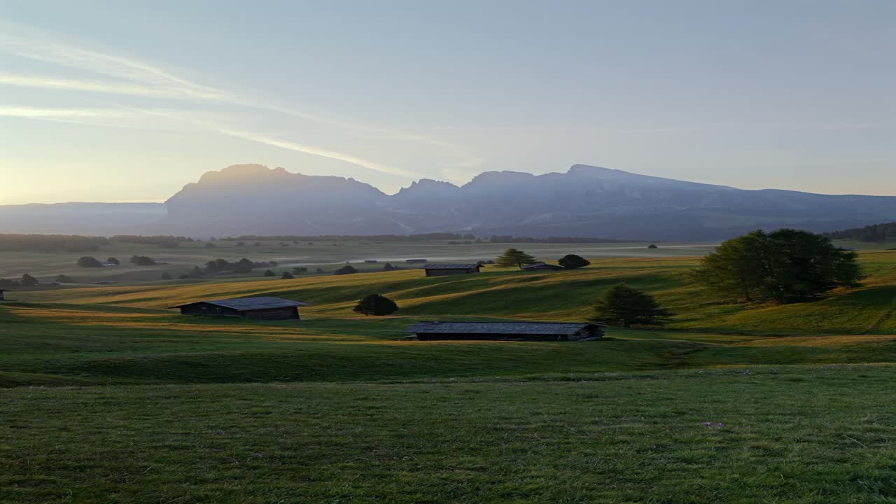 Vertical shot of the Alpe di Siusi at sunset, capturing the Dolomites’ towering peaks and scenic meadow landscape dotted with rustic mountain huts in South Tyrol, Italy.