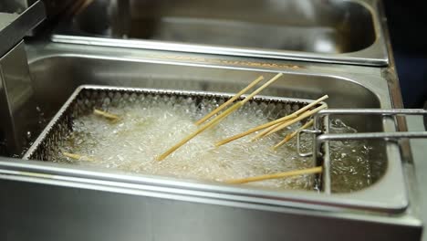 food being deep fried on skewers in a commercial fryer.