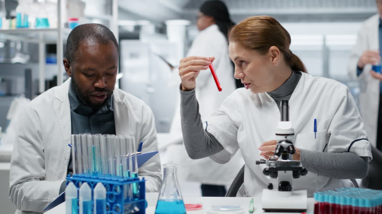 Pathologist examining biopsy slide while colleague documents diagnostic findings