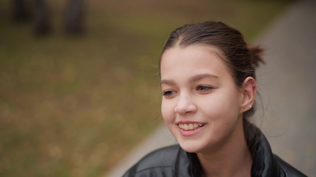 Close up of young woman adjusting her black glasses with long manicured nails while wearing leather jacket. scene is set outdoors on pathway surrounded by green grass captured in soft
