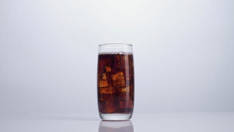 ice cubes falling in a glass of fresh cola on white background