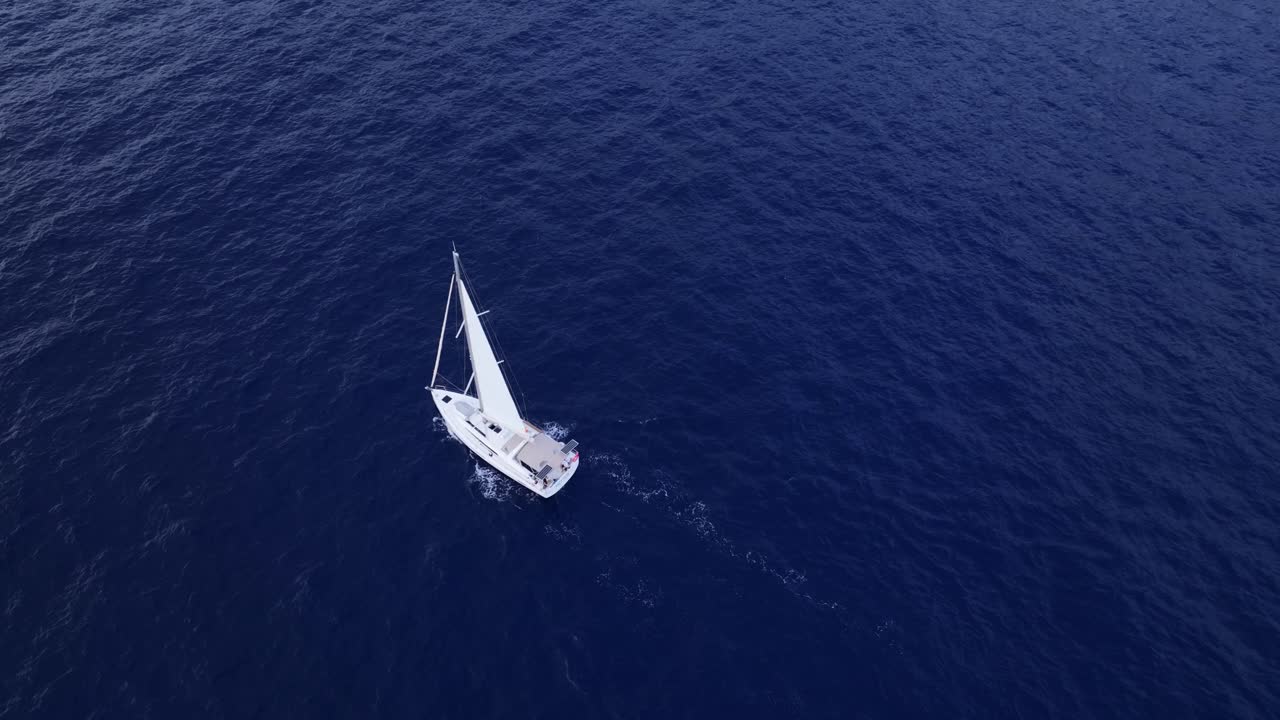 White sailboat gracefully moving through calm, deep blue waters, drone descends