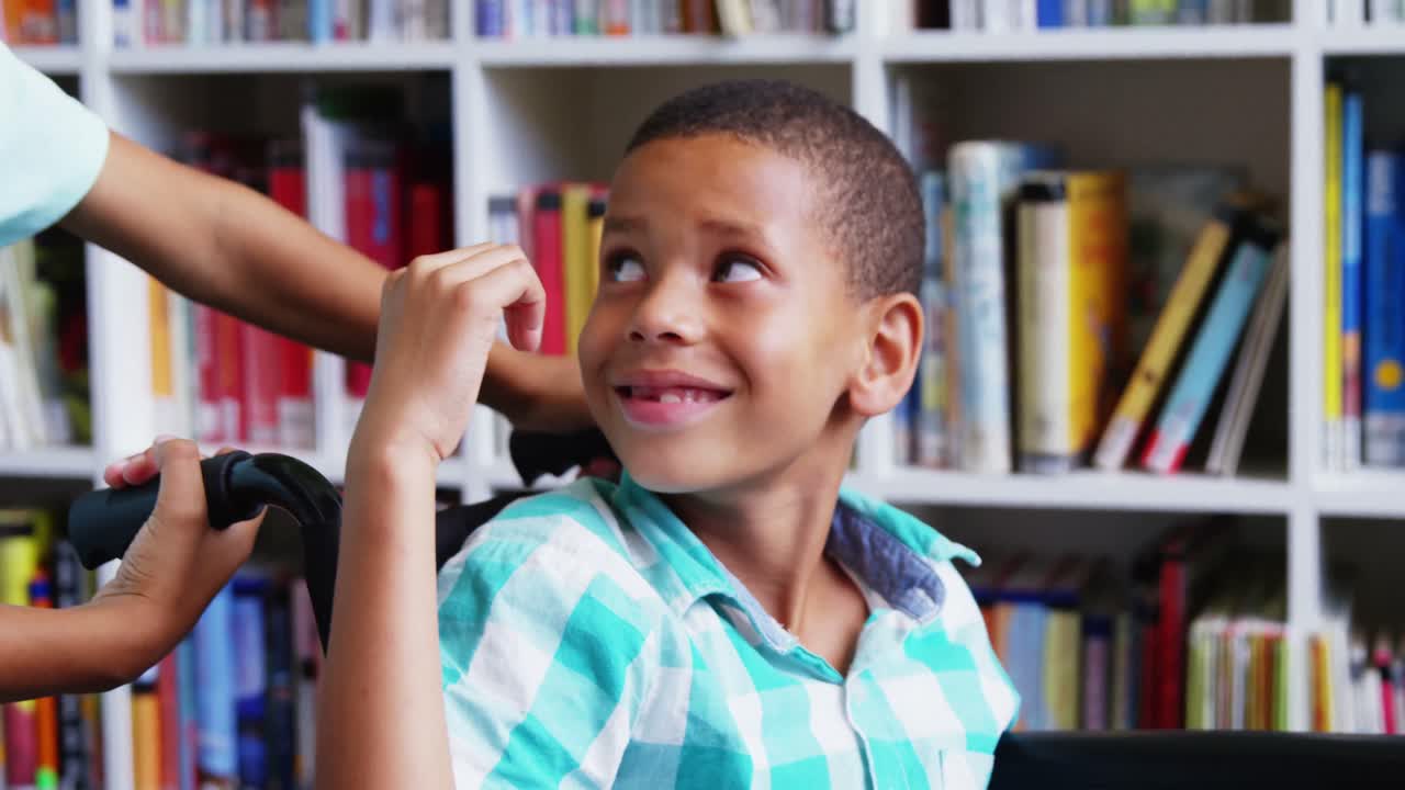 Happy schoolboy carrying his friend in wheelchair at library