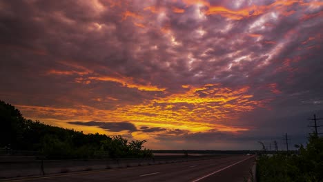 Golden-hour-bright-red-and-yellow-green-rays-illuminate-epic-clouds-and-pierce-sky-above-busy-highway