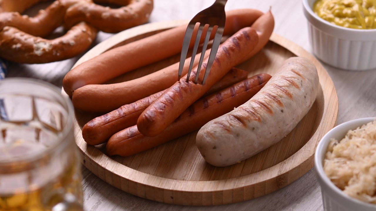 Plockar upp en grillad korv med en gaffel från en tallrik
