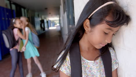 in school, girl with backpack feeling sad while other girls whispering nearby