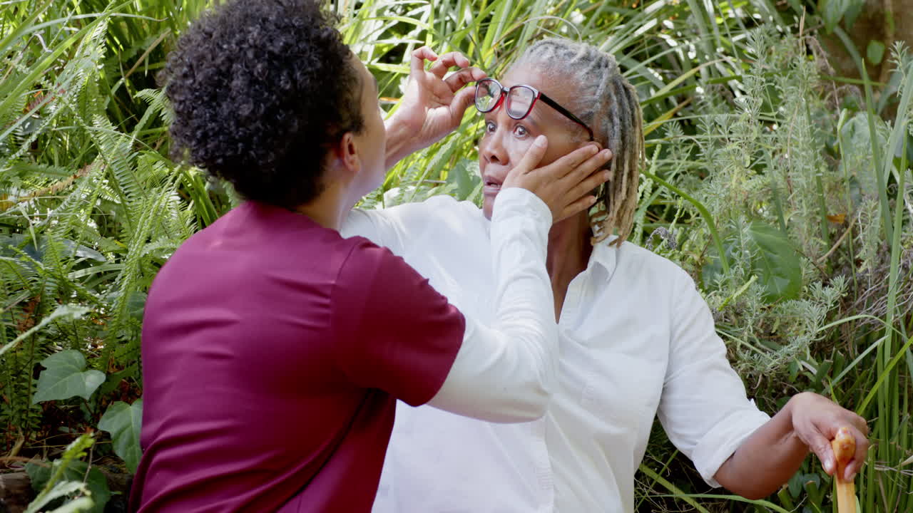 Caregiver assisting senior woman with glasses adjustment in garden setting