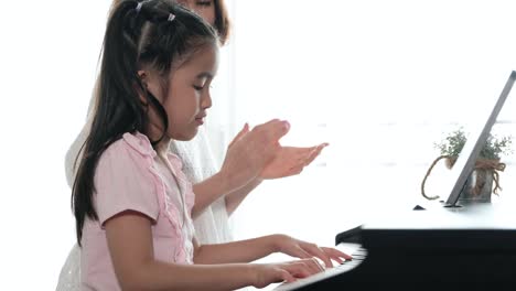 slow motion footage of asian mother and her daughter playing piano together. mother teaching daughter with happiness and smile, clapping her hands.