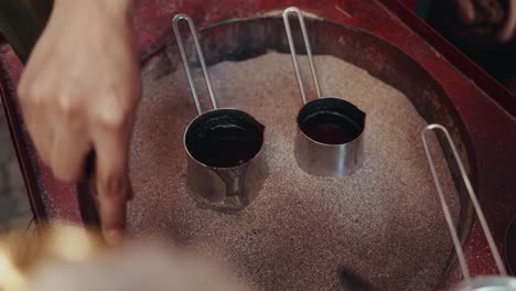 close up shot of turkish coffee on traditional pots being prepared on hot sand