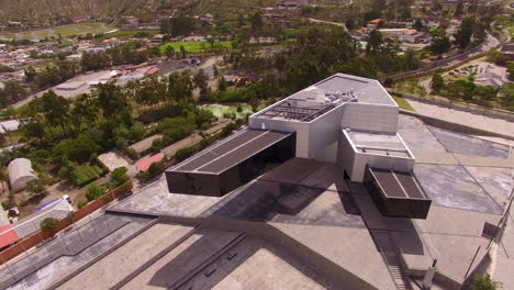 drone displaying a large modern building with a ecuadorian mountain city in the distance