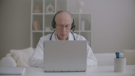 male doctor is consulting online colleagues and patients elderly male therapist is sitting at office in clinic and chatting online