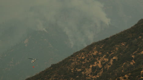 helicopter deploying water to fight a wildfire on a smoky mountainside